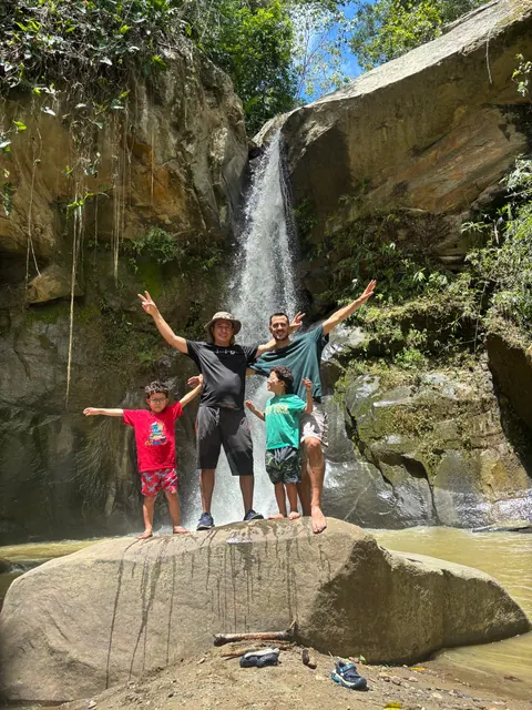 Eine Familie mit erhobenen Armen vor dem Wasserfall am Fluss, Puerto Alejandría